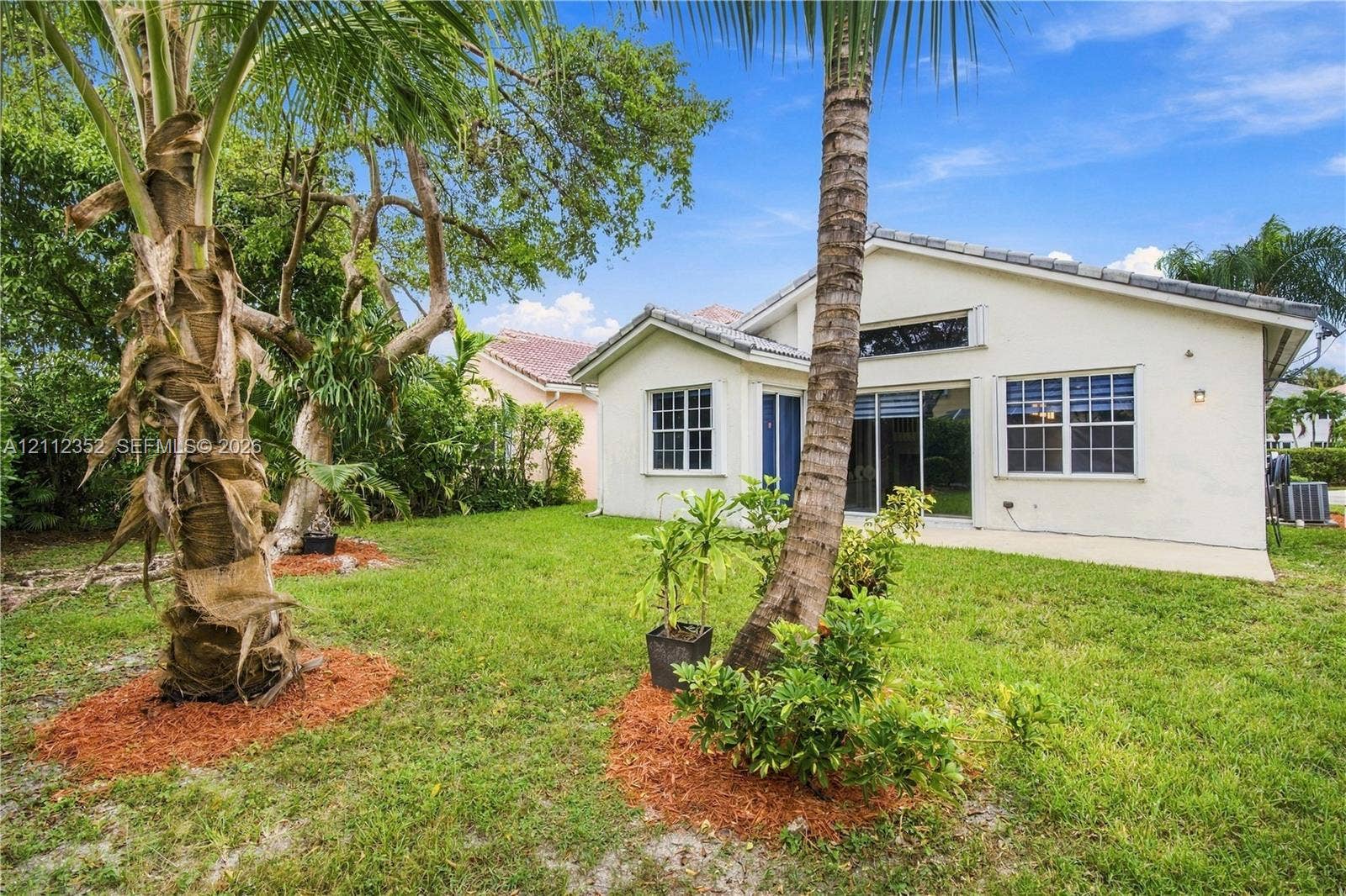 2880 NW 75th Avenue, Margate, FL 33063 Rear exterior featuring stucco siding, multi-pane windows, sliding glass door, and mature palm trees