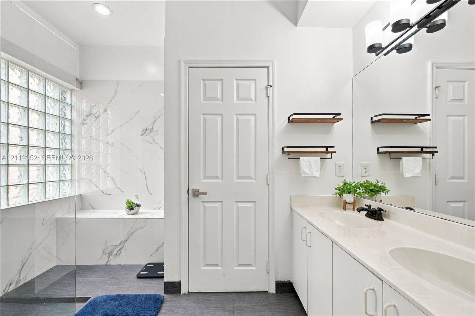 2880 NW 75th Avenue, Margate, FL 33063 Bathroom featuring a walk-in shower with stone-finish surround, glass block window, double vanity with solid surface countertop, and matte black fixtures