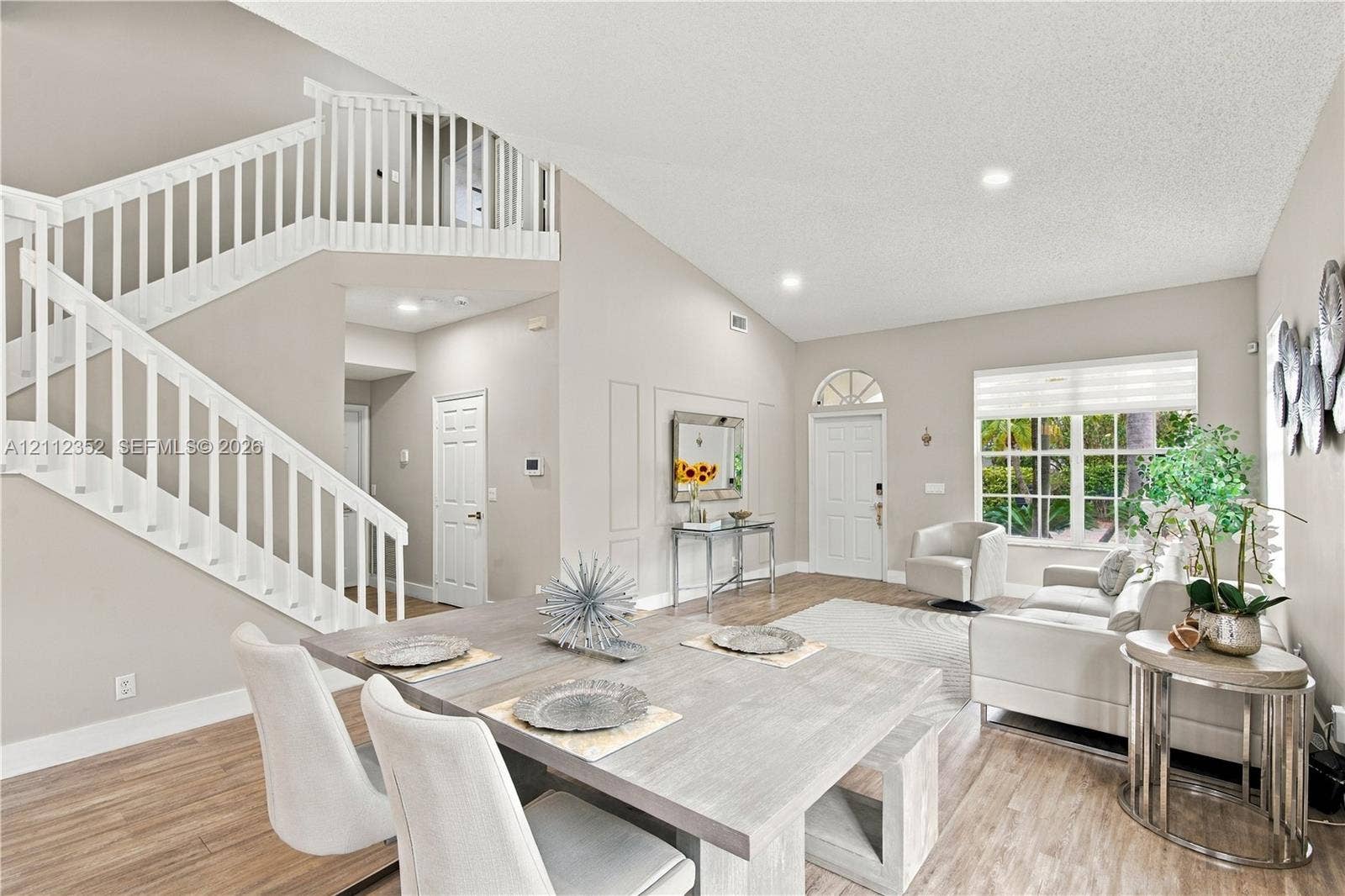 2880 NW 75th Avenue, Margate, FL 33063 Open-concept interior featuring vaulted ceilings, wood-finish flooring, a white staircase with decorative balustrade, and multi-paned windows with a transom