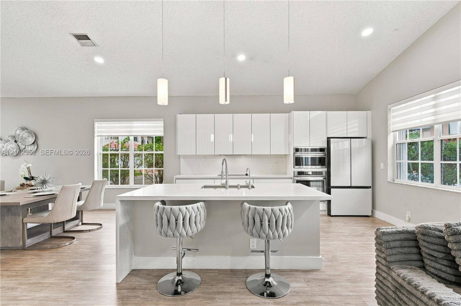 2880 NW 75th Avenue, Margate, FL 33063 Modern kitchen featuring gloss-finish cabinetry, a white countertop island with an undermount sink, three pendant lights, built-in stainless steel appliances, and wood-finish flooring