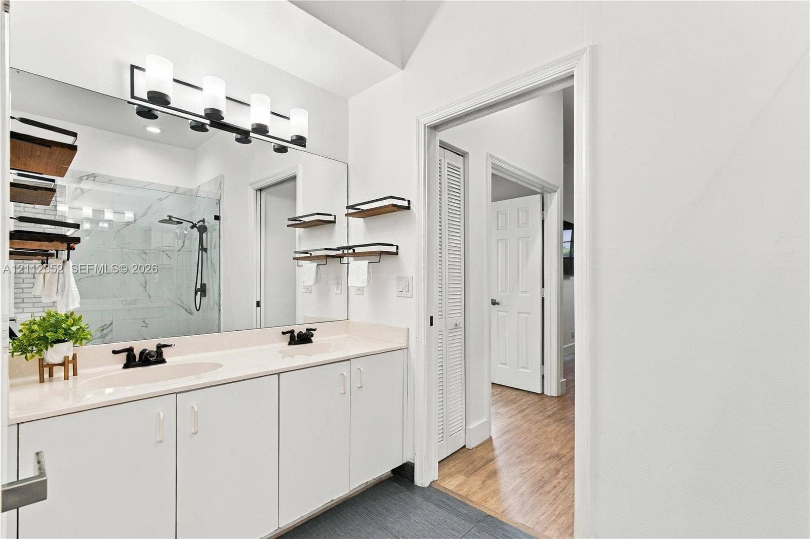 2880 NW 75th Avenue, Margate, FL 33063 Dual-sink vanity with solid-surface countertop, full-width wall mirror, four-light vanity fixture, matte black hardware, and shower featuring large-format wall tile