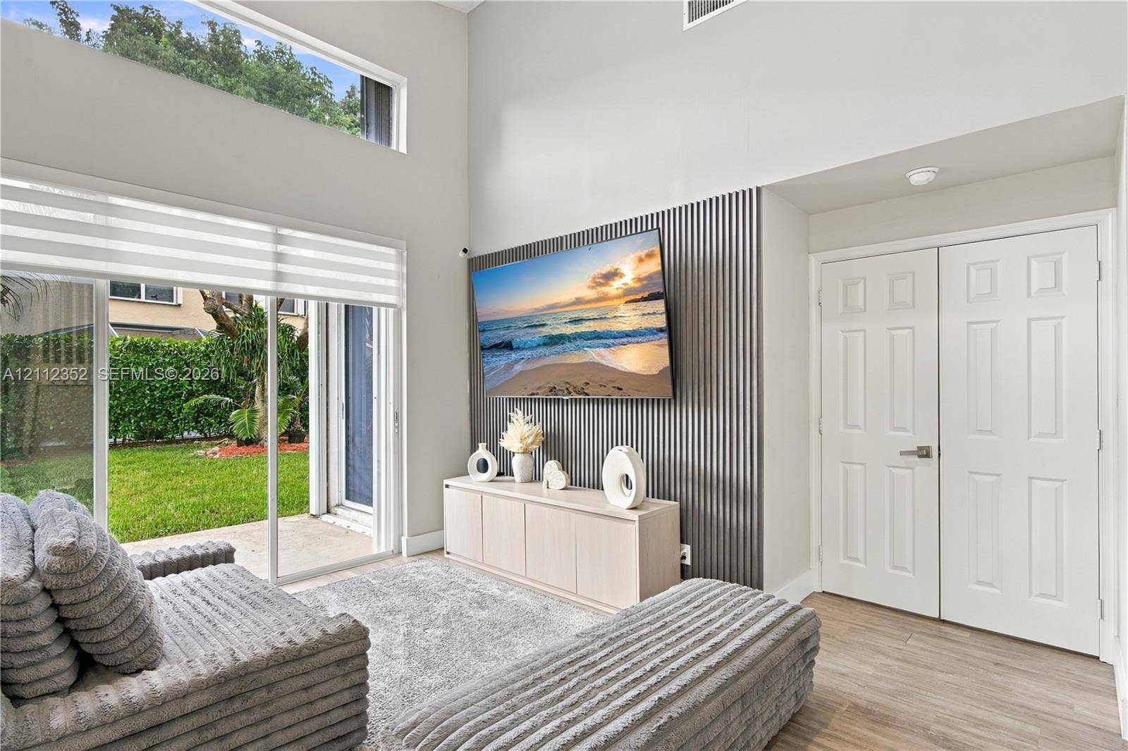 2880 NW 75th Avenue, Margate, FL 33063 High-ceiling room featuring double-height windows, vertical slat wall paneling, sliding glass doors, and light-tone wood-finish flooring