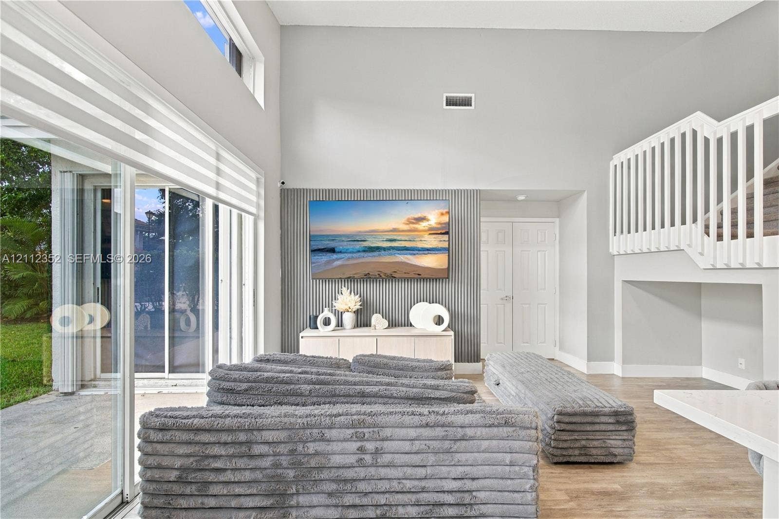 2880 NW 75th Avenue, Margate, FL 33063 Vaulted ceilings featuring expansive sliding glass doors, a ribbed accent wall, wood-finish flooring, and a mezzanine staircase with white balusters