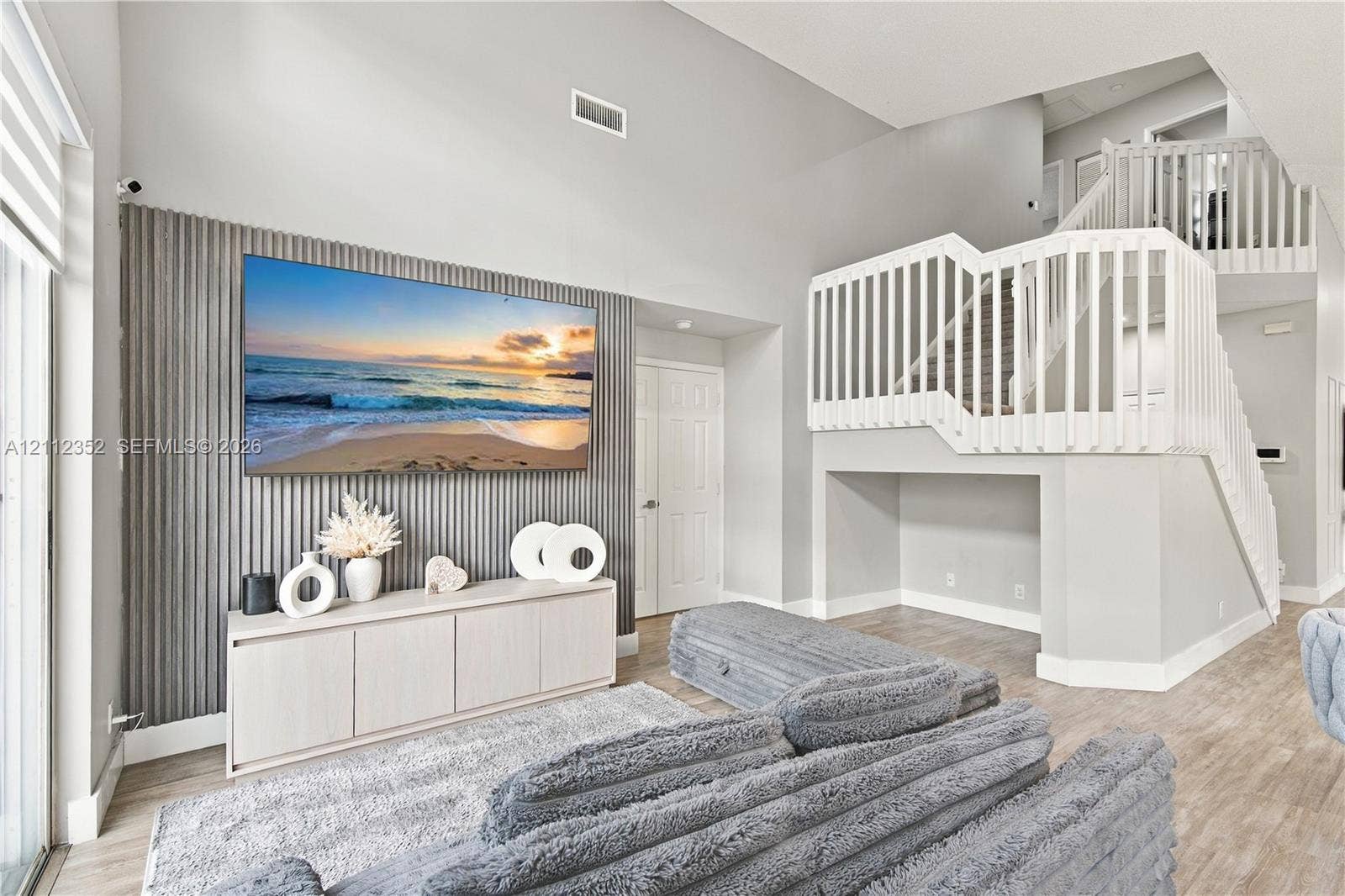 2880 NW 75th Avenue, Margate, FL 33063 High-ceiling living area featuring a ribbed accent wall, wood-finish flooring, and a staircase with white vertical balusters