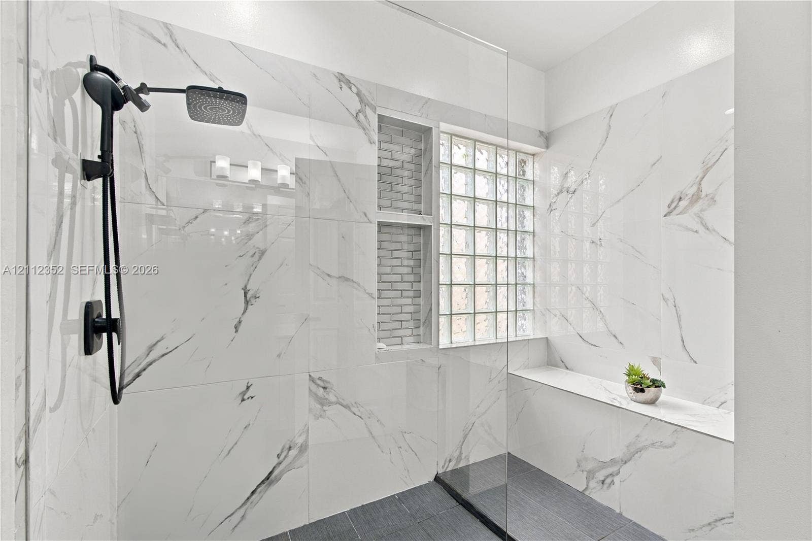 2880 NW 75th Avenue, Margate, FL 33063 Walk-in shower featuring large-format stone-patterned wall tiles, dark floor tile, a glass partition, a built-in bench, and a matte black rainfall showerhead