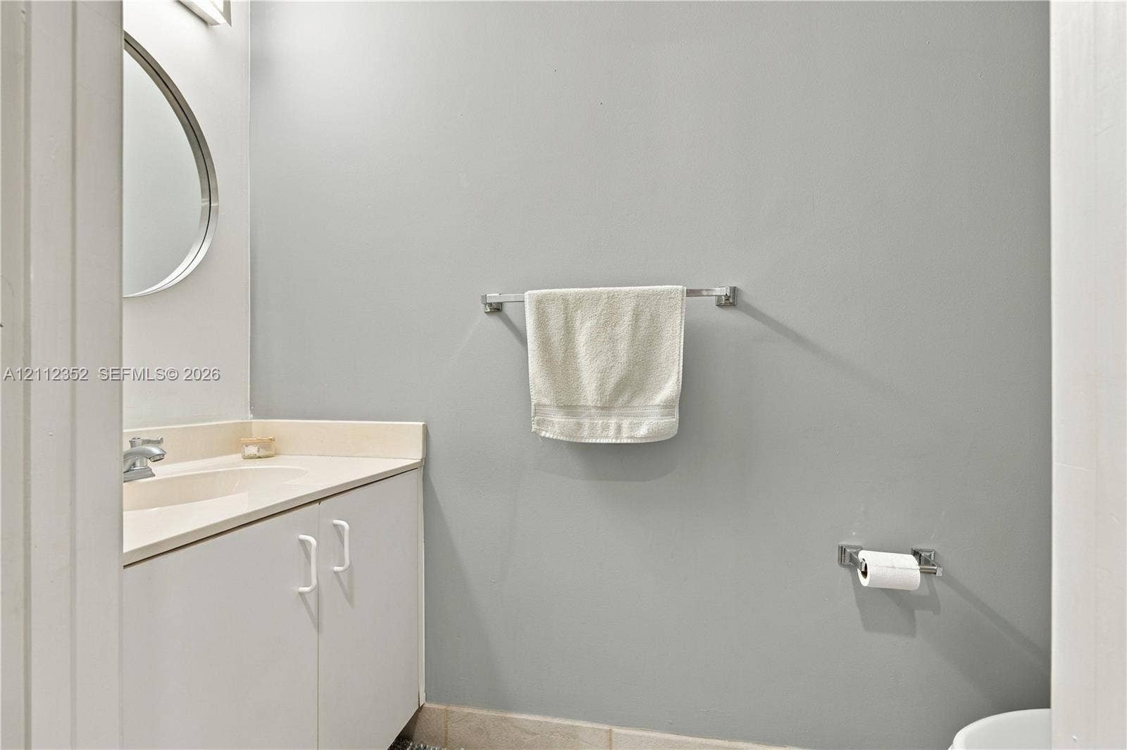 2880 NW 75th Avenue, Margate, FL 33063 Bathroom featuring a vanity with an integrated sink, polished chrome faucet, wall-mounted circular mirror, and chrome hardware fixtures
