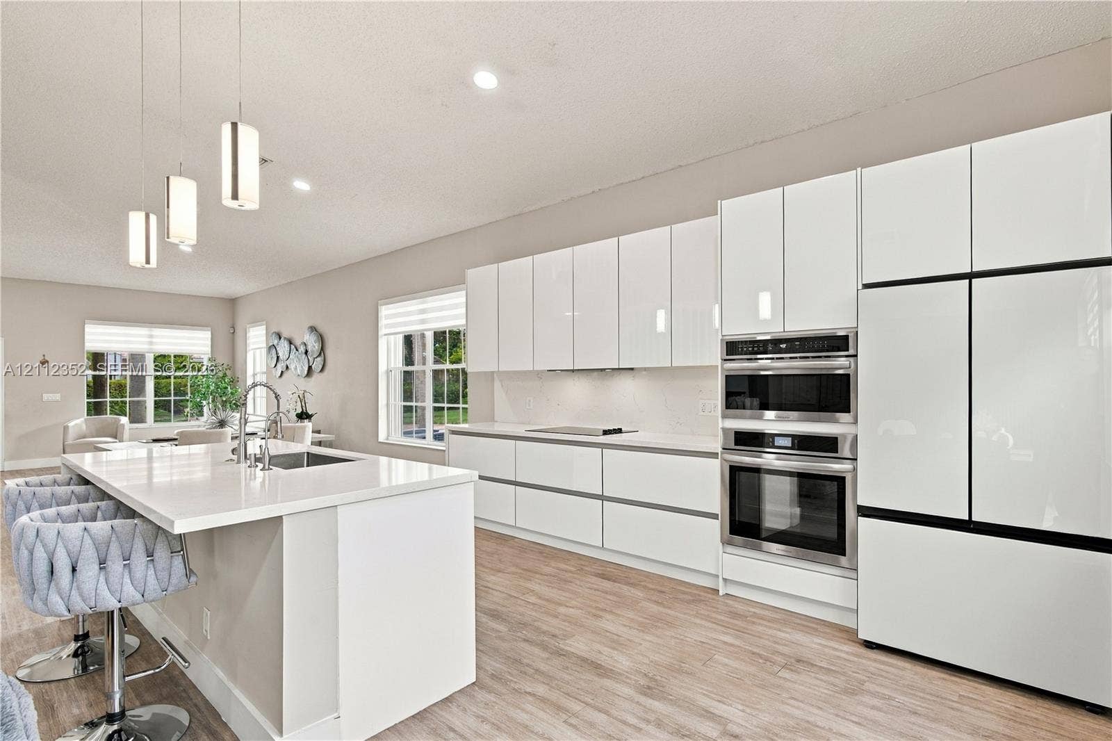 2880 NW 75th Avenue, Margate, FL 33063 Kitchen featuring high-gloss white cabinetry, white stone-surface countertops, wood-finish flooring, built-in stainless steel appliances, and three glass pendant lights