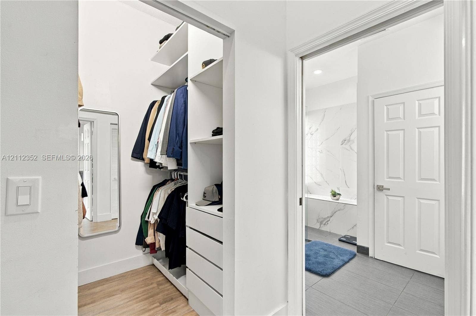 2880 NW 75th Avenue, Margate, FL 33063 Walk-in closet featuring custom white shelving, integrated drawers, and wood-finish flooring, accompanied by a bathroom showcasing a stone-tile shower surround and large-format floor tile