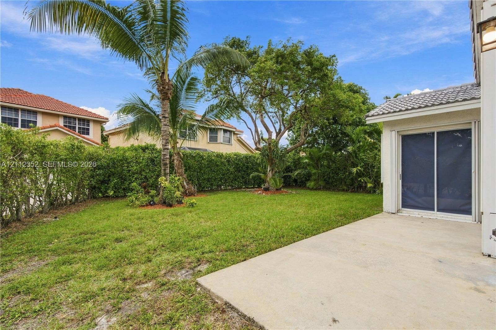 2880 NW 75th Avenue, Margate, FL 33063 Backyard featuring a concrete patio, manicured lawn, established palm tree, and perimeter shrubbery