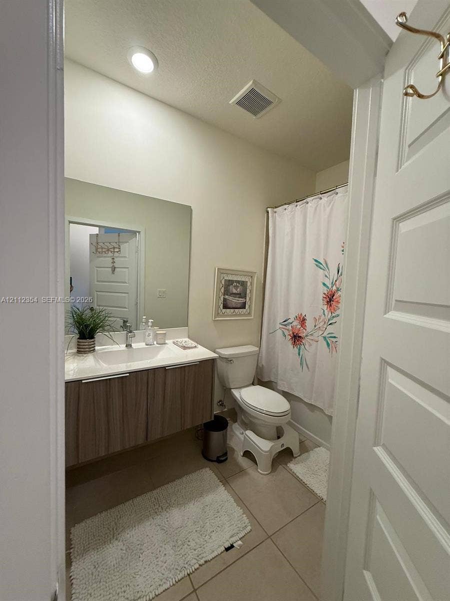 Floating vanity with a light wood-finish cabinet, white countertop, integrated sink, large wall-mounted mirror, and tile flooring