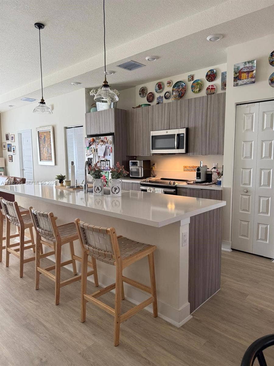 Kitchen featuring an expansive island with a light-toned solid surface countertop, wood-finish cabinetry, built-in microwave, recessed lighting, and pendant fixtures