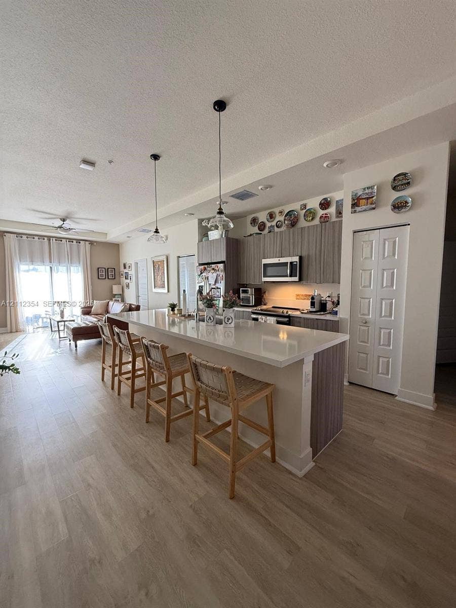 Open-concept kitchen featuring an expansive quartz-topped island, vertical-grain cabinetry, pendant lighting, and wood-finish flooring