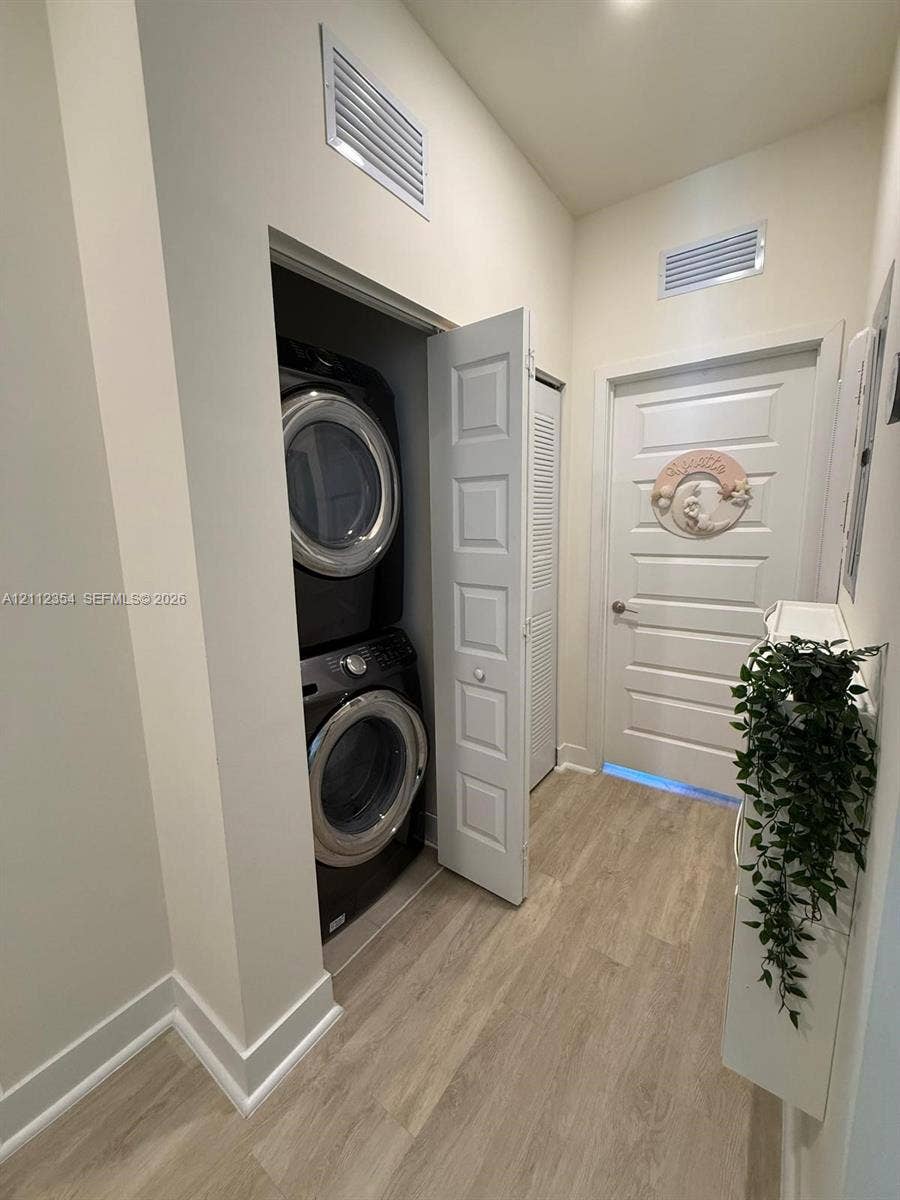 Laundry area featuring wood-finish flooring, a stacked appliance unit, and a five-panel interior door