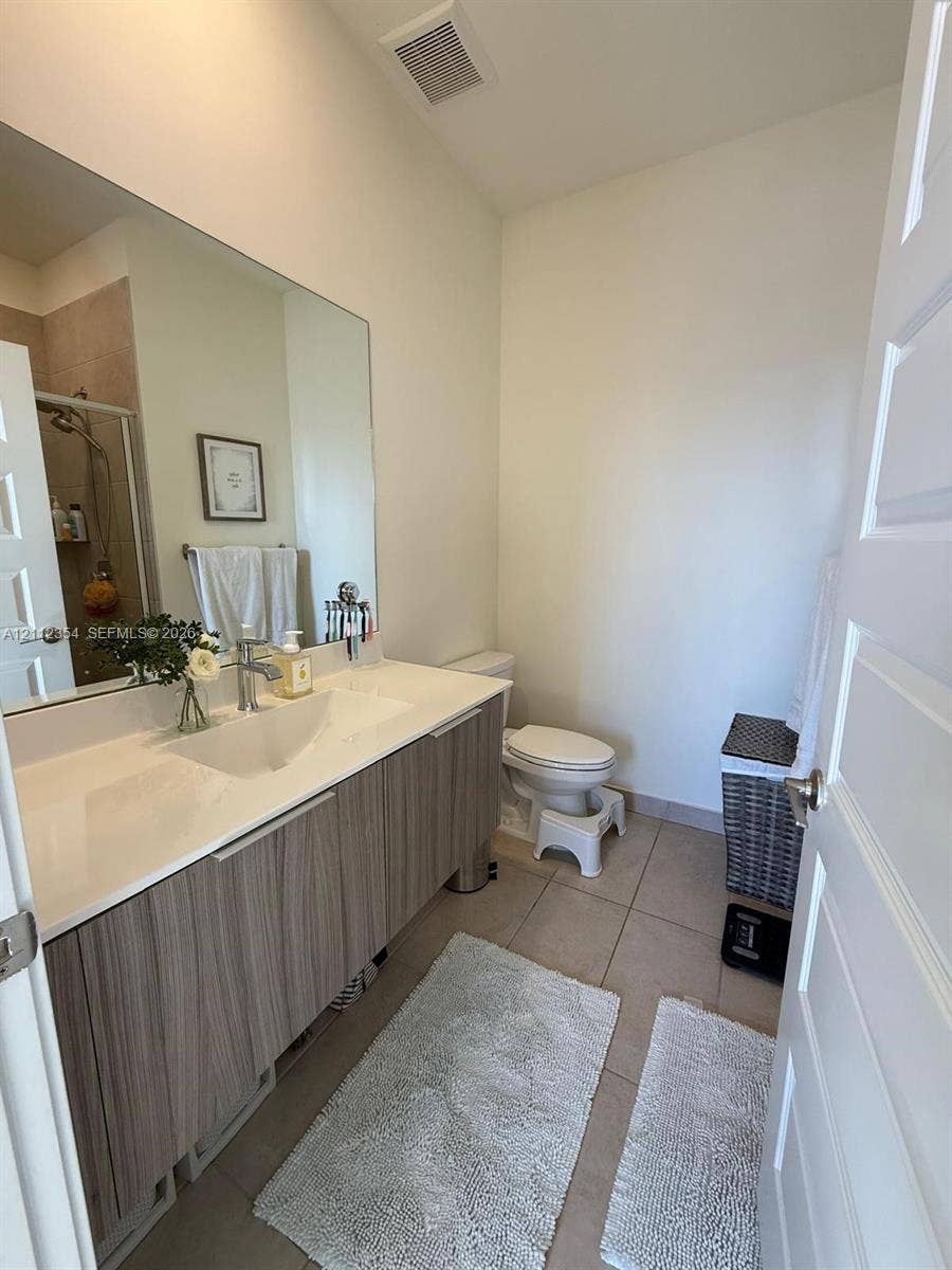 Floating vanity with wood-finish cabinetry, integrated countertop with a molded sink, polished chrome faucet, large-format mirror, and tile flooring