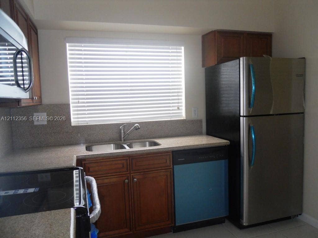 Kitchen featuring wood cabinetry, stone-surface countertops, dual-basin sink, integrated stainless steel appliances, and horizontal window blinds