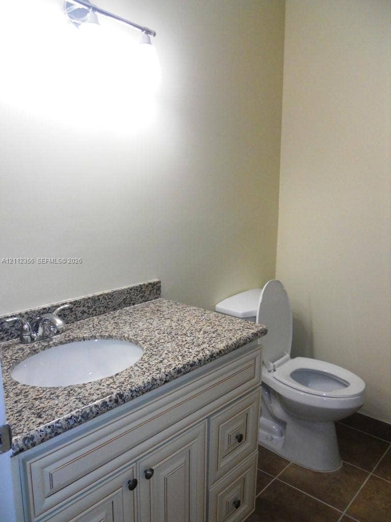 Bathroom featuring a vanity with stone-finish countertop, undermount sink, chrome faucet, decorative panel cabinetry, and tiled flooring