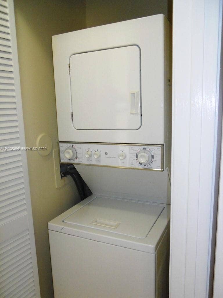 Stacked laundry unit with top-loading washer, front-loading dryer, and white louvered closet door