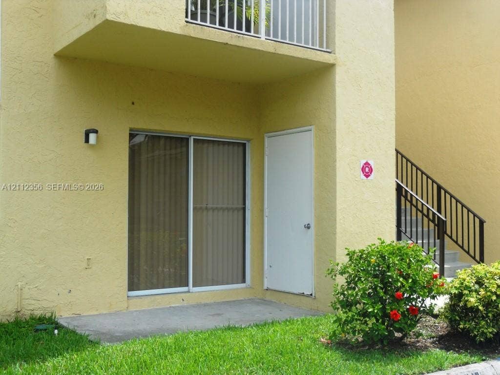 Stucco exterior featuring a concrete patio, sliding glass door, private exterior storage closet, and second-story balcony with metal railing