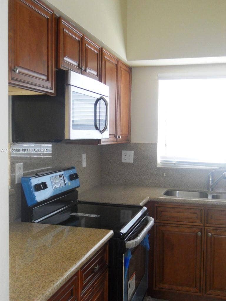 Kitchen featuring stained wood cabinetry, stone countertops, stainless steel over-the-range microwave, black electric range, and dual-basin undermount sink