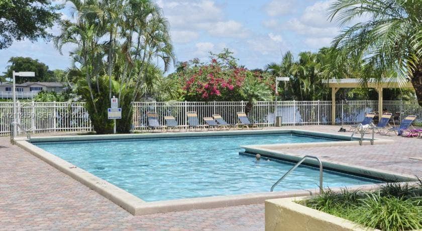 In-ground swimming pool featuring a paver deck, metal fencing, and an attached covered pavilion