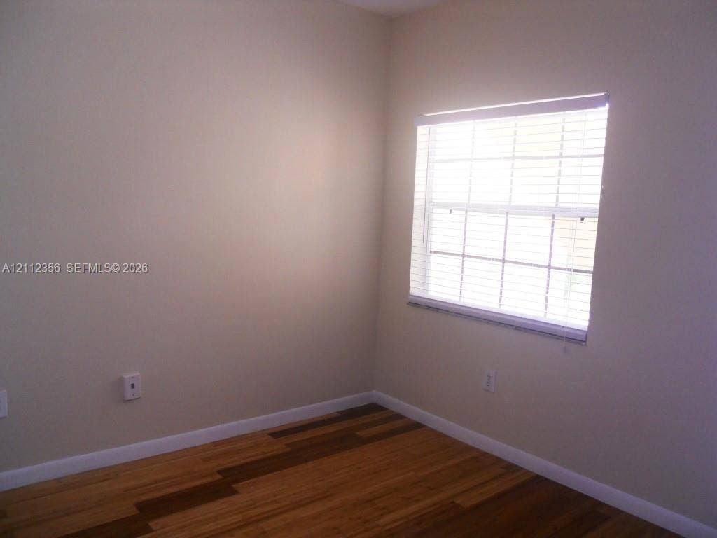 Room featuring wood-finish flooring, neutral wall paint, and a window fitted with horizontal blinds