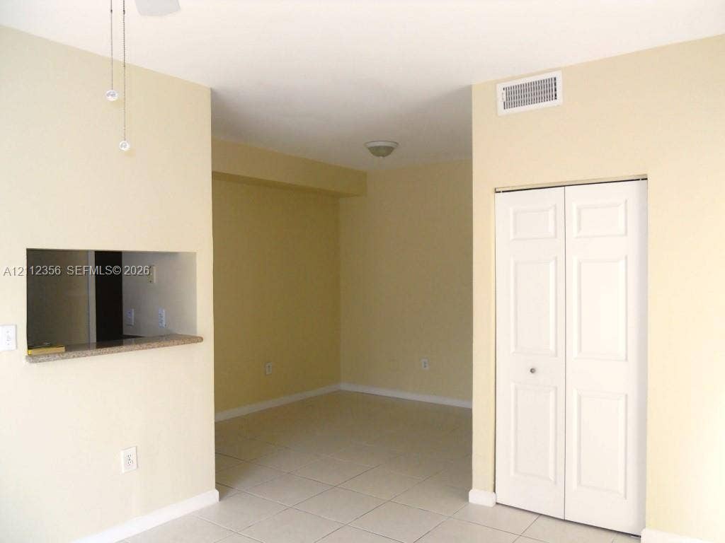 Neutral-toned interior space featuring light-colored tile flooring, a built-in pass-through opening with a stone-finish countertop, and a white bi-fold closet door