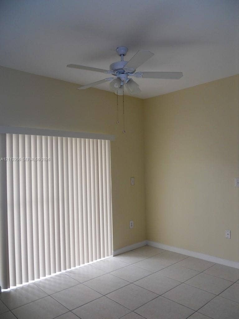 Room featuring ceramic tile flooring, a multi-blade ceiling fan with integrated lighting, and a vertical sliding glass door with blinds