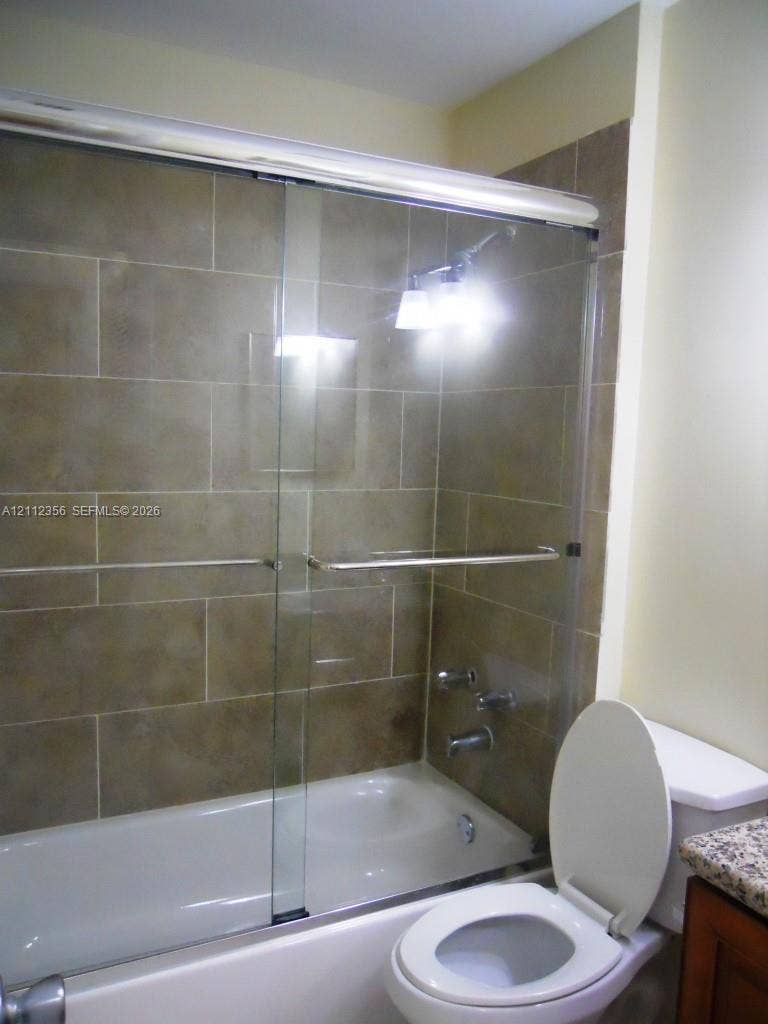 Bathtub featuring a glass sliding door and large-format rectangular wall tile, complemented by a stone-finish countertop