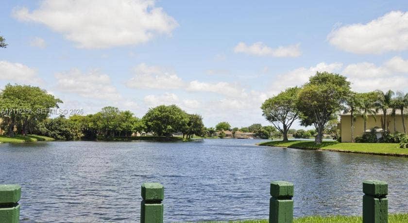 Waterfront property featuring a pond, manicured turf, and mature trees