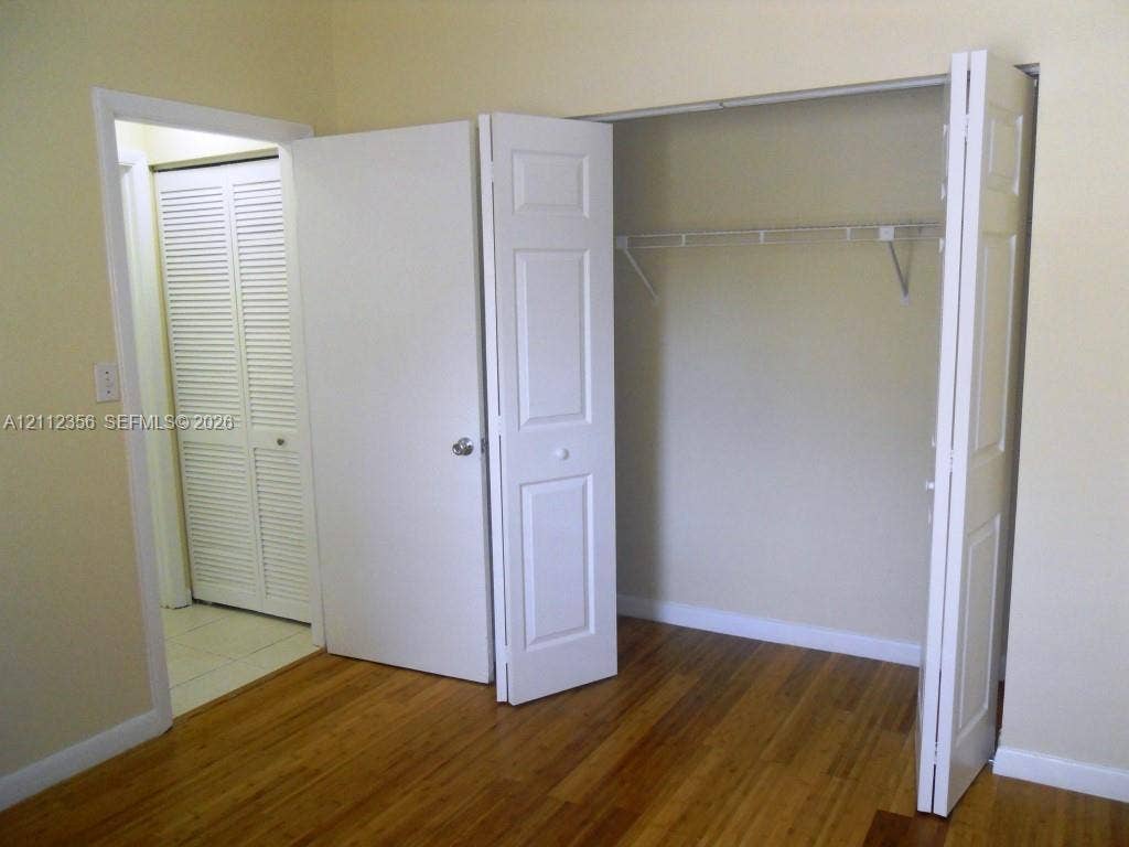 Wood-finish flooring, white panel bi-fold closet doors, integrated wire shelving, and white louvered doors