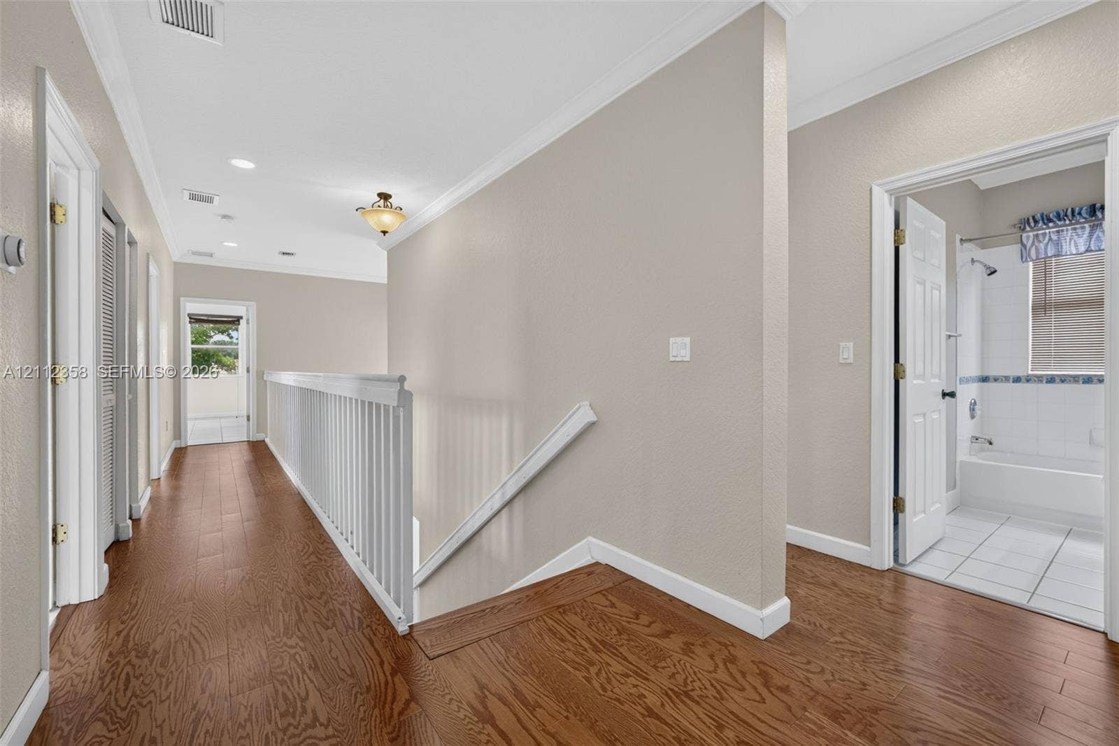 1611 SE 16th Street, Homestead, FL 33035 Hallway featuring wood-finish flooring, white crown molding, a decorative ceiling-mounted light fixture, and a white balustrade