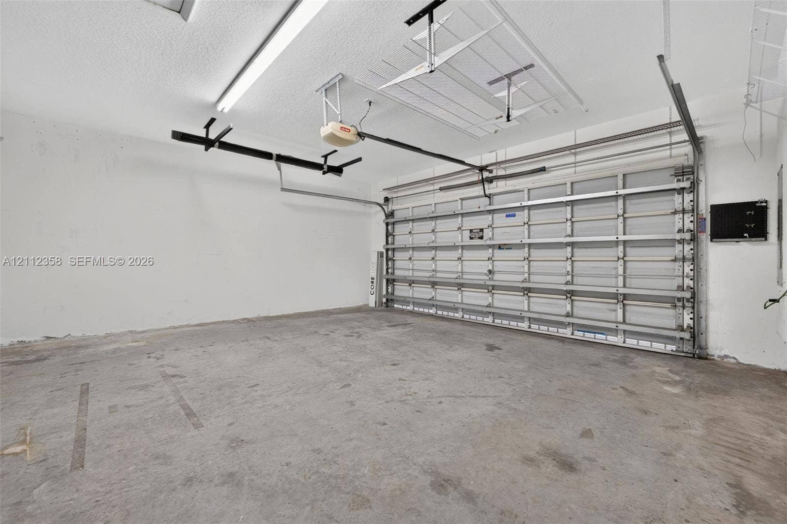 1611 SE 16th Street, Homestead, FL 33035 Two-car garage featuring a sectional metal roll-up door, automated door opener, finished interior walls, and overhead lighting