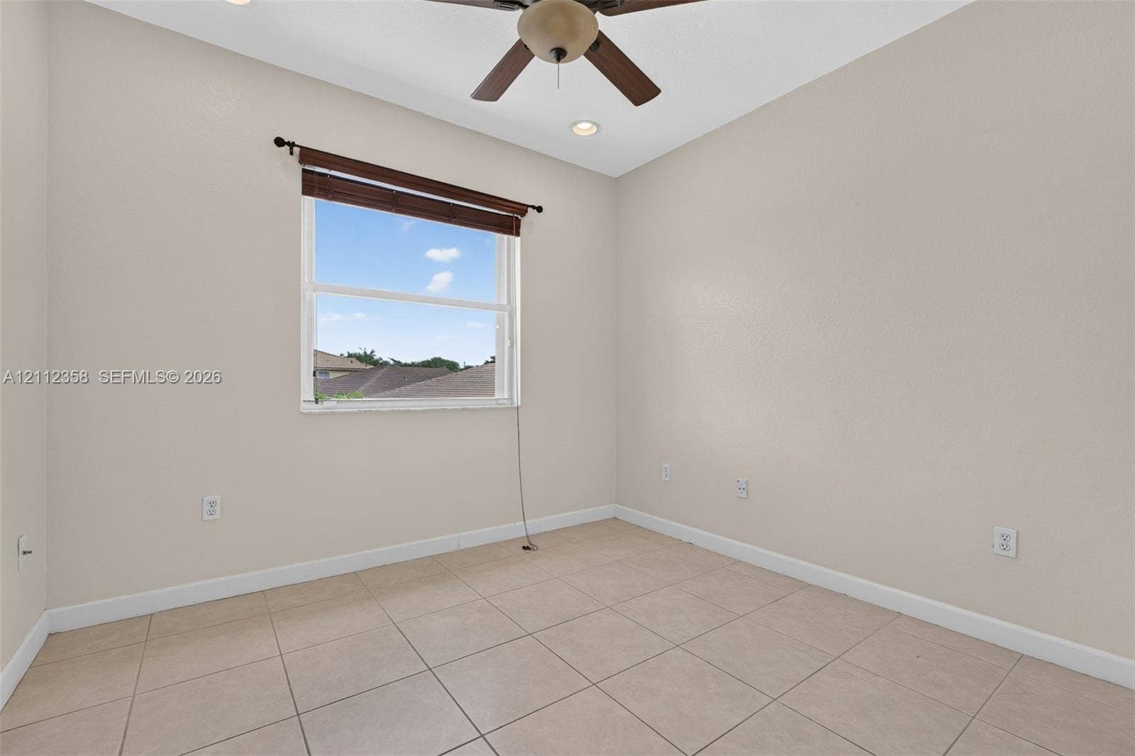 1611 SE 16th Street, Homestead, FL 33035 Neutral-toned interior space featuring tile flooring, a ceiling fan with integrated lighting, and a single-pane window with a roller shade