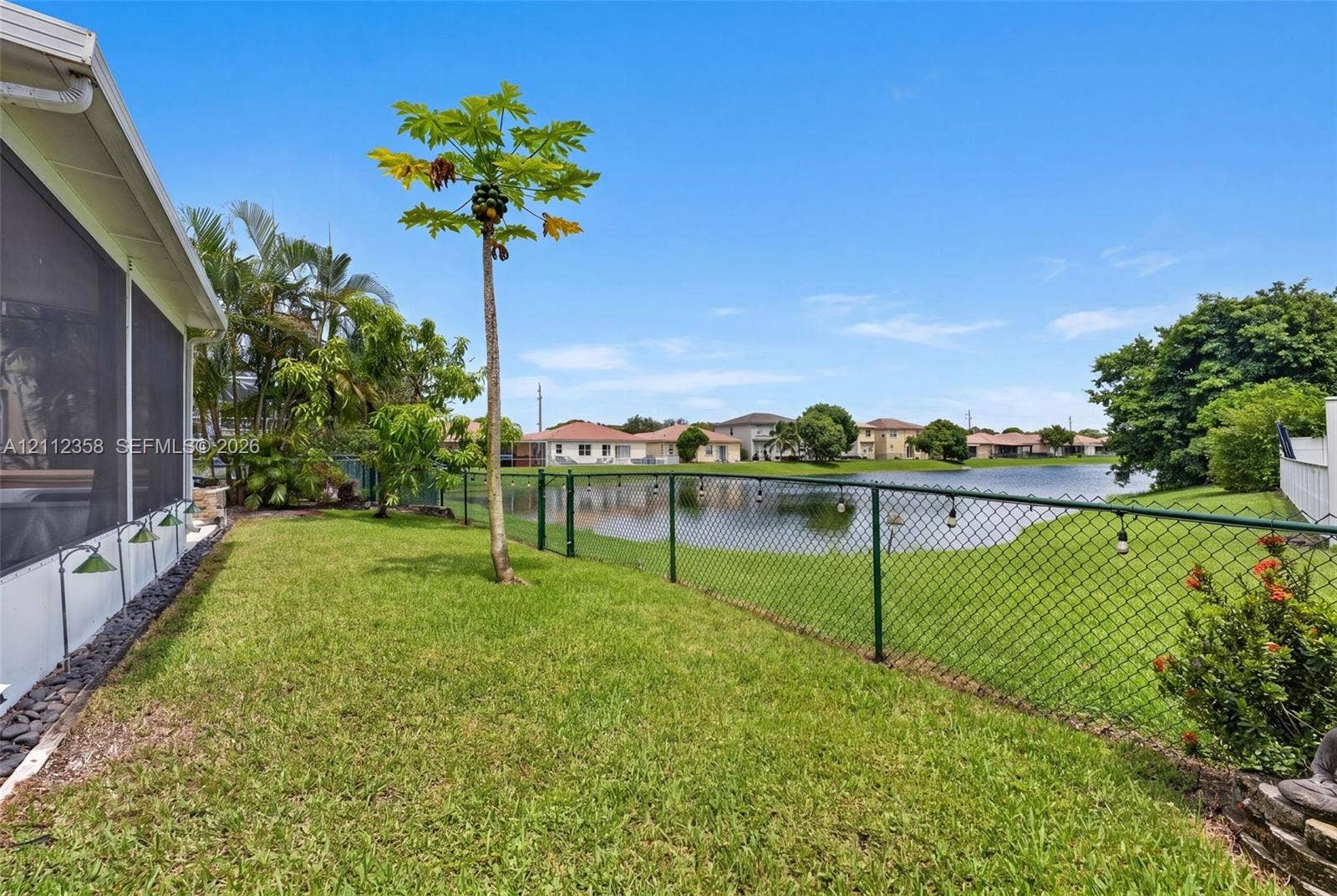 1611 SE 16th Street, Homestead, FL 33035 Backyard featuring a manicured lawn, water frontage, metal chain-link fencing, and mature landscaping