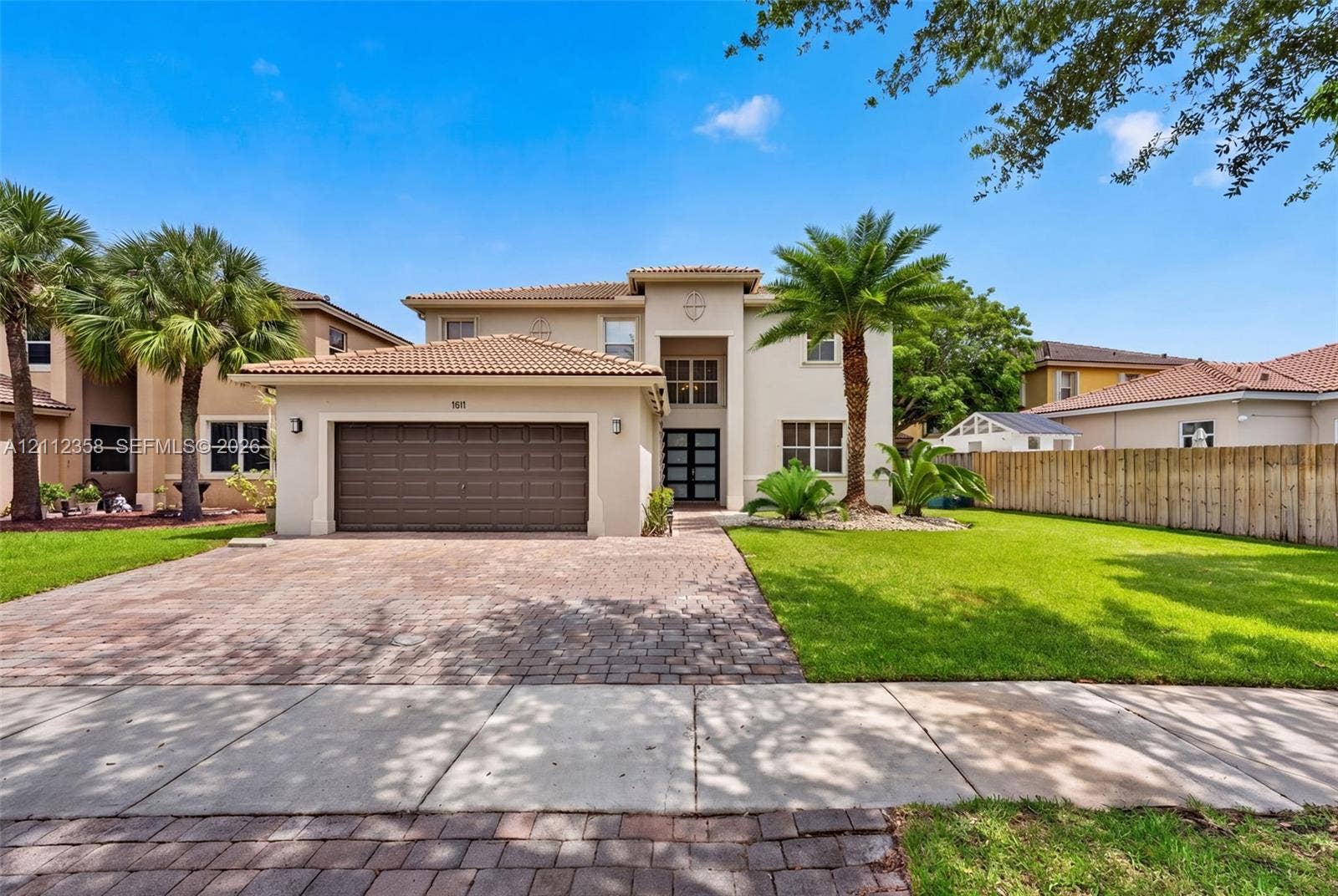 1611 SE 16th Street, Homestead, FL 33035 Stucco exterior featuring a dual-pitch tile roof, paver driveway, attached two-car garage, and manicured landscaping