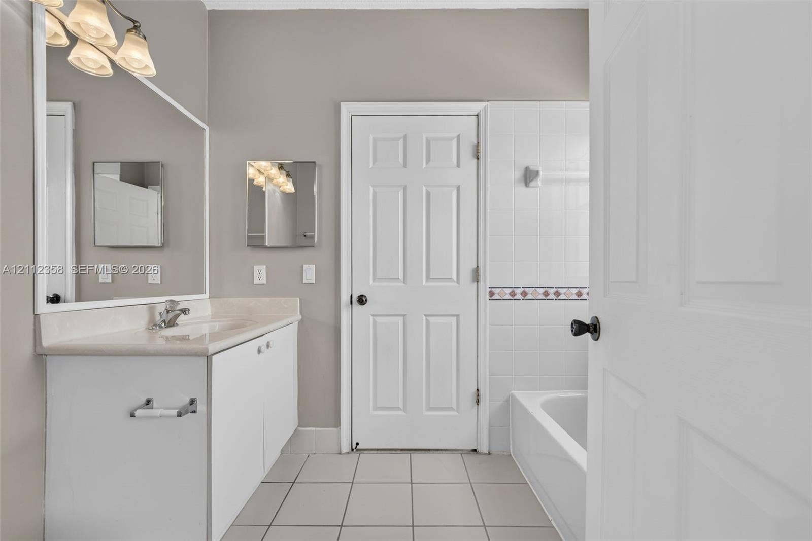 1611 SE 16th Street, Homestead, FL 33035 Bathroom featuring a white vanity with a stone countertop, a large wall-mounted mirror, a multi-bulb light fixture, a tiled shower-tub combination, and neutral ceramic tile flooring