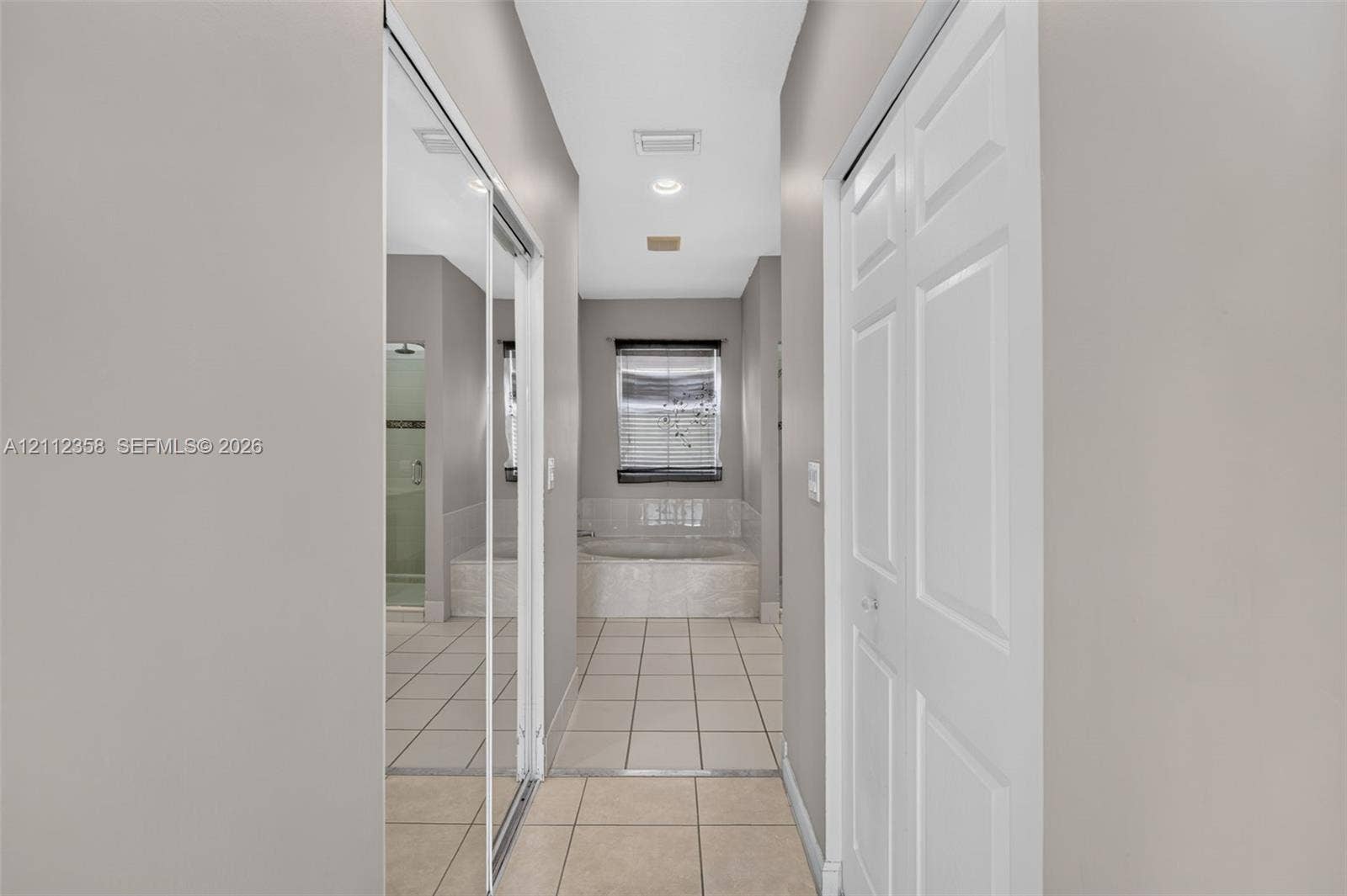 1611 SE 16th Street, Homestead, FL 33035 Hallway featuring mirrored sliding closet doors, white six-panel door, recessed lighting, and tile flooring with access to a tile-surround soaking tub
