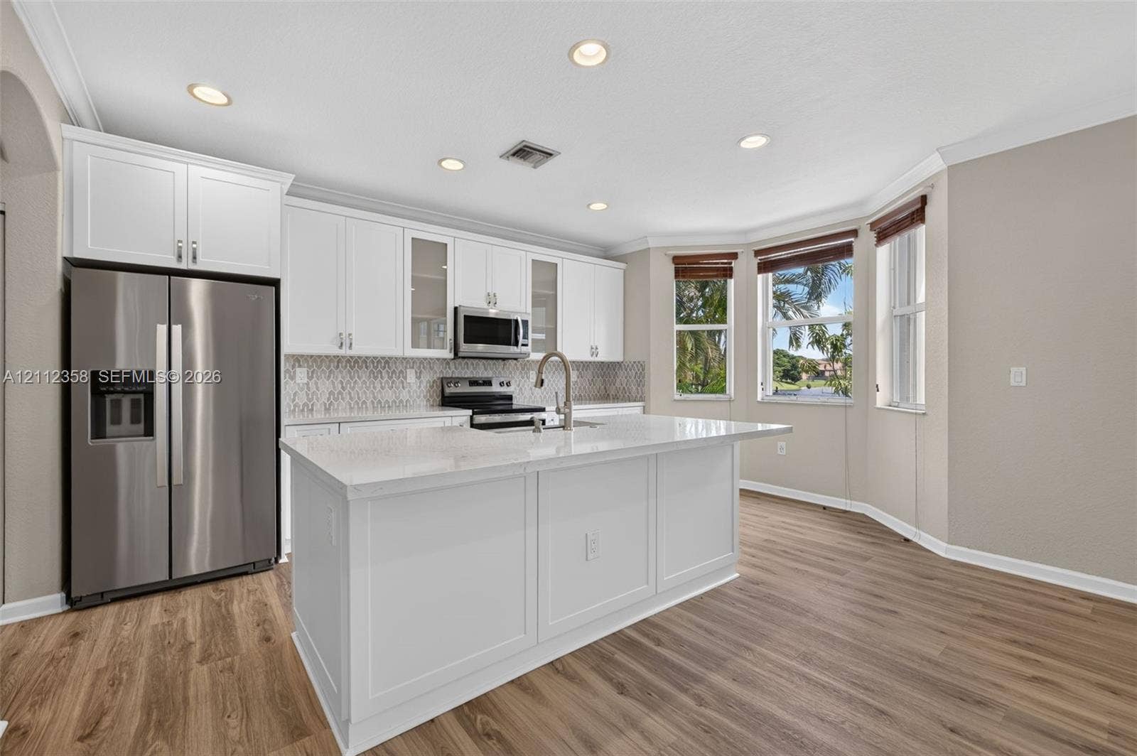 1611 SE 16th Street, Homestead, FL 33035 Kitchen featuring white cabinetry with glass-front display panels, stone-finish countertops, stainless steel appliances, a center island with a built-in sink, and wood-finish flooring