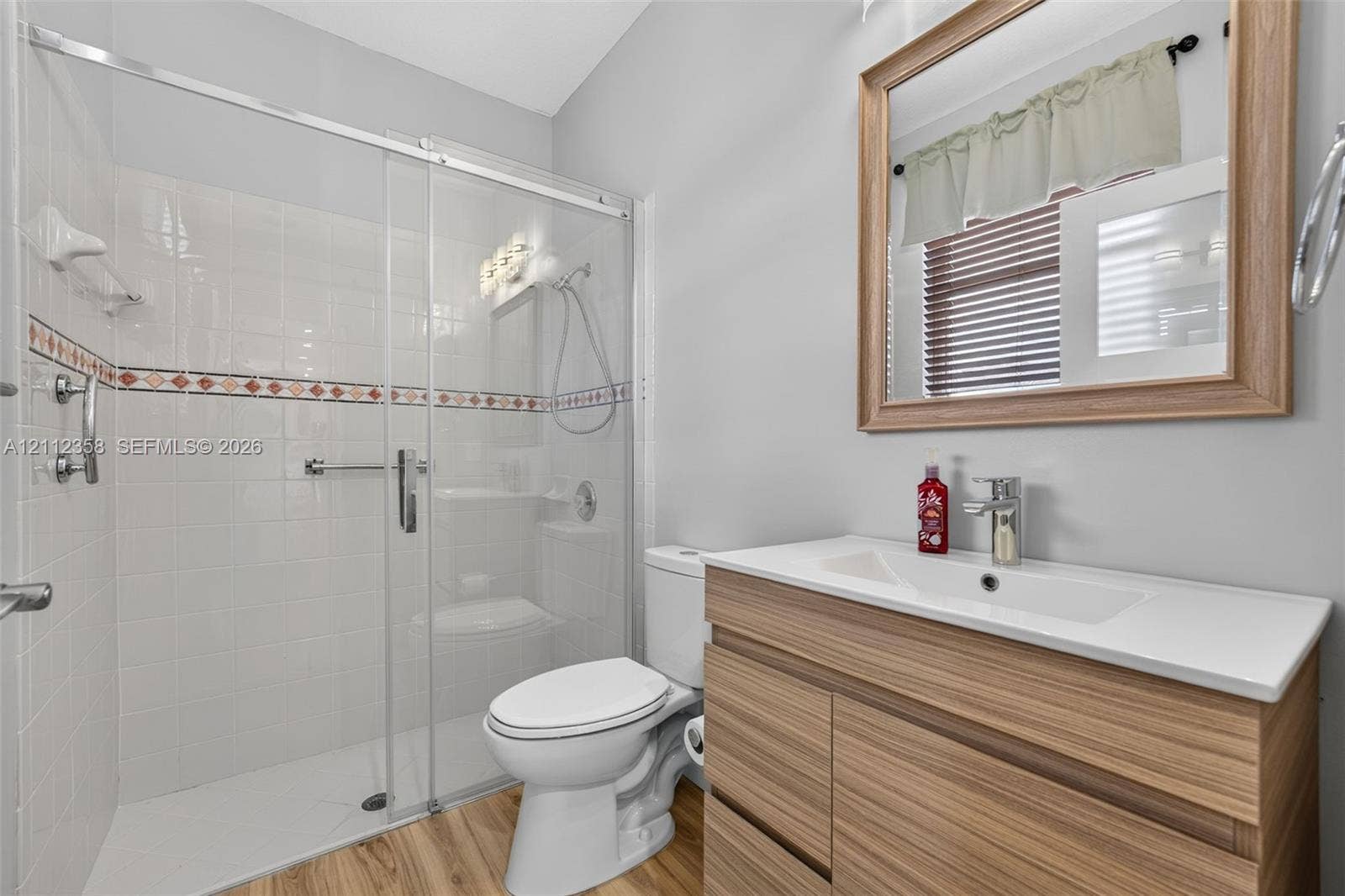 1611 SE 16th Street, Homestead, FL 33035 Bathroom featuring a wood-finish vanity with a rectangular sink, walk-in glass-enclosed shower with tile surround, wood-finish flooring, and a framed wall mirror