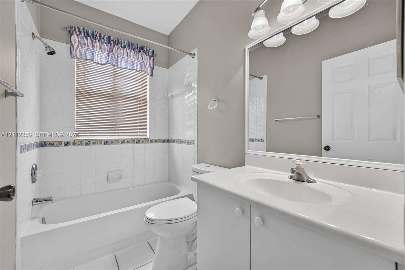 1611 SE 16th Street, Homestead, FL 33035 Bathroom featuring a white vanity with an integrated basin, a large wall-mounted mirror, a tub-shower combination with ceramic tile surround, and tile flooring