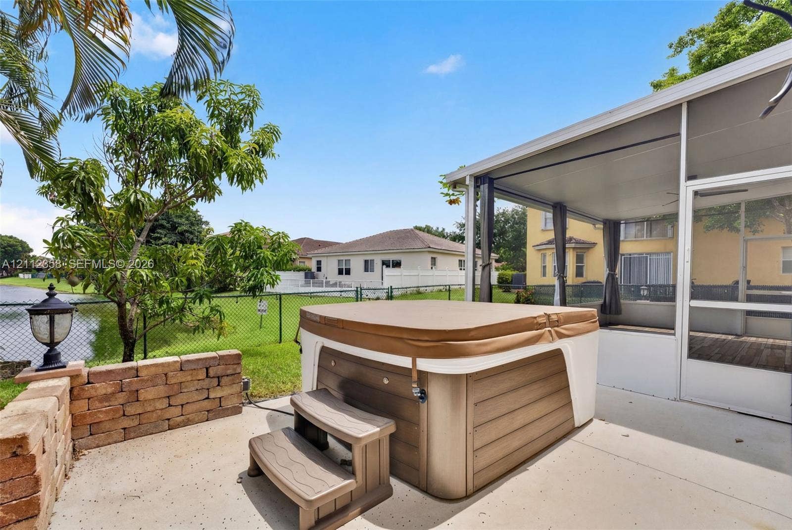 1611 SE 16th Street, Homestead, FL 33035 Screened-in patio with a concrete deck, built-in hot tub, brick retaining wall, and fenced backyard bordering water