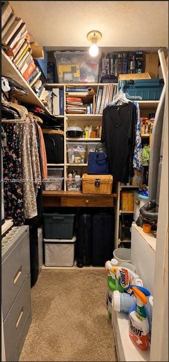 Storage space featuring floor-to-ceiling built-in shelving, a dedicated wooden work surface with a drawer, and overhead lighting