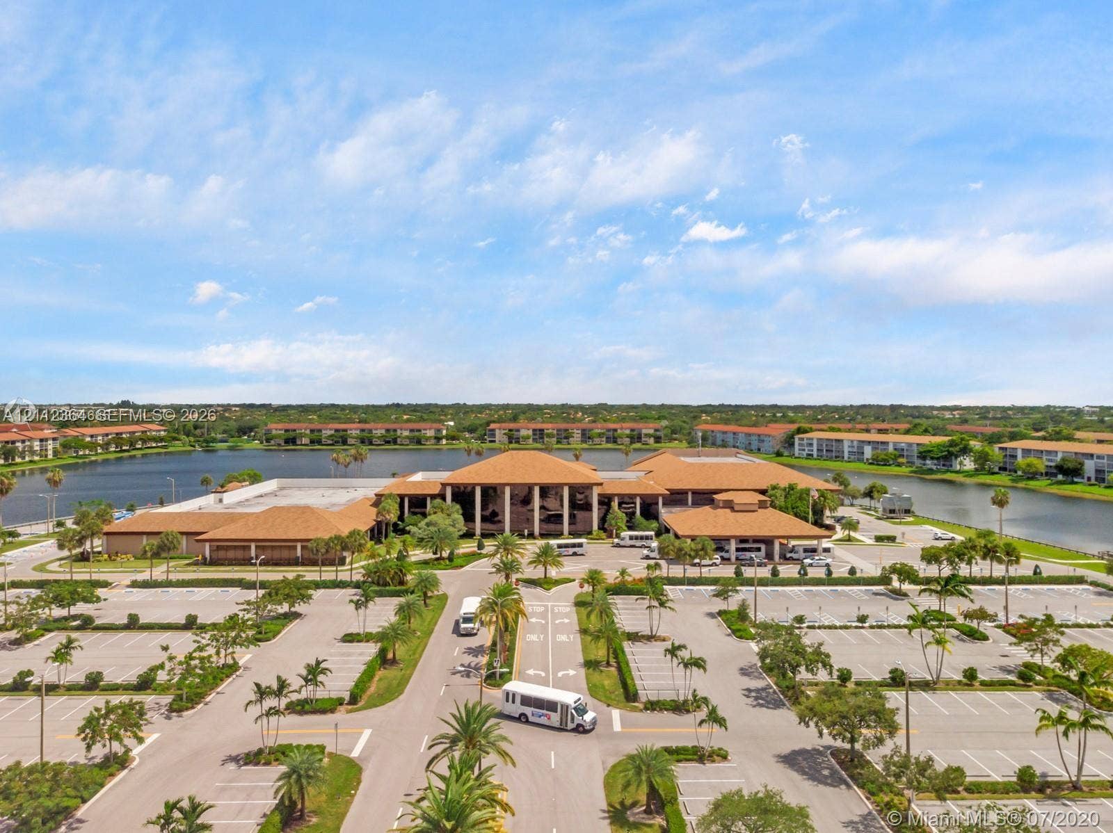 Aerial view of a sprawling complex featuring multiple low-rise buildings, expansive parking facilities, mature palm trees, and waterfront grounds