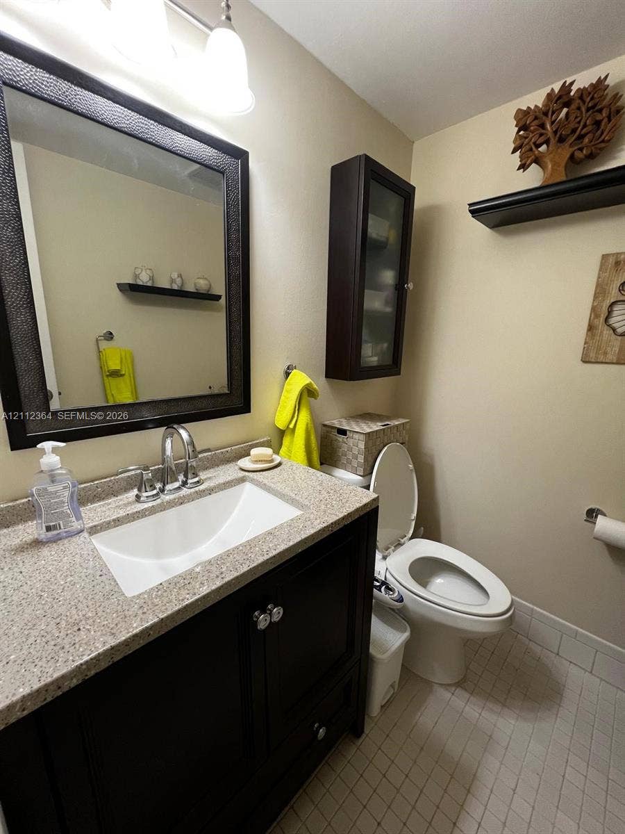 Dark wood vanity with integrated basin and stone-composite countertop, wall-mounted storage cabinetry, framed wall mirror, and neutral tile flooring