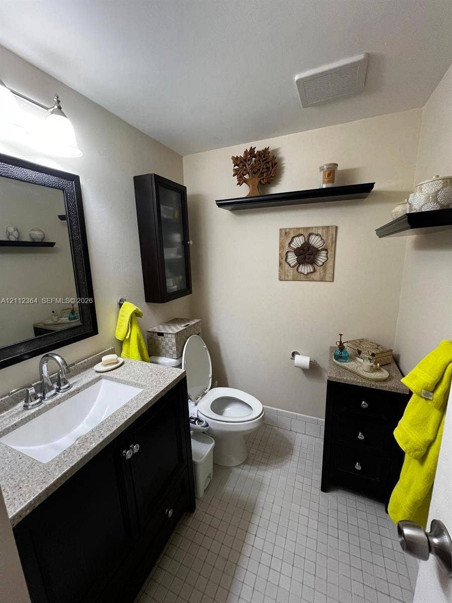 Dark wood vanity with a stone-finish countertop, integrated sink, wall-mounted storage cabinet, and white tile flooring