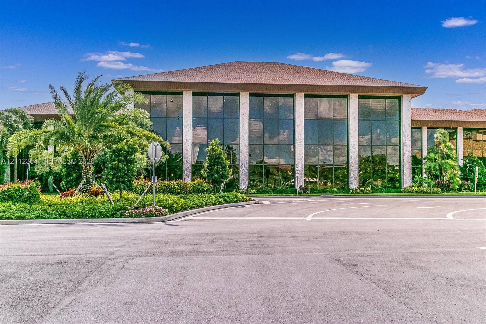 Commercial building exterior featuring extensive glass wall panels, structured stone columns, and a hipped roofline, surrounded by manicured landscaping