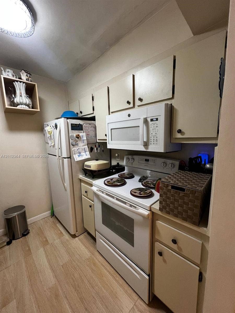 Kitchen featuring flat-panel cabinetry, wood-finish flooring, built-in over-the-range microwave, and white appliances