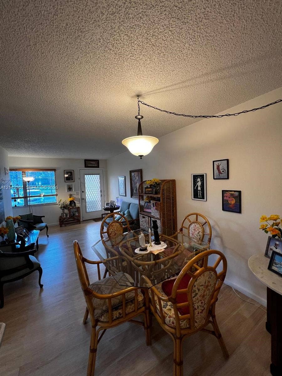 Open-concept interior featuring wood-finish flooring, a pendant light fixture, and a white exterior door with a decorative metal storm door