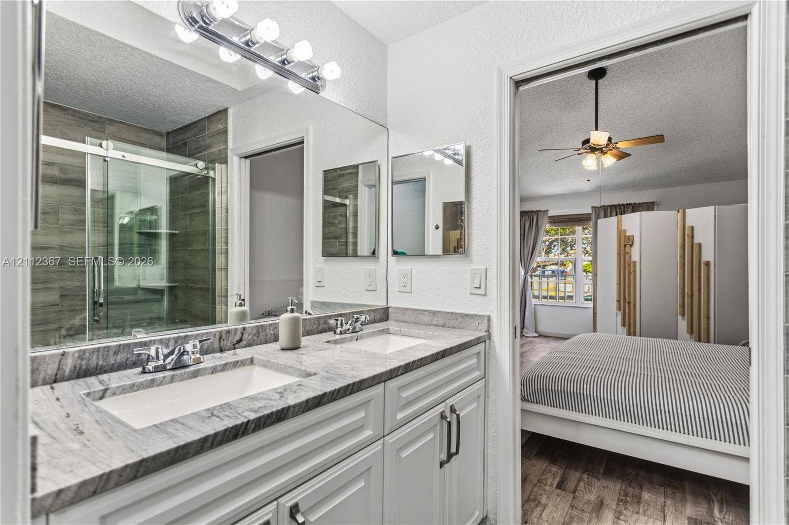 10803 Cypress Glen Drive, #10803, Coral Springs, FL 33071 Bathroom featuring a dual-sink vanity with stone countertop, oversized wall-to-wall mirror, glass-enclosed shower with tiled surround, and integrated cabinetry