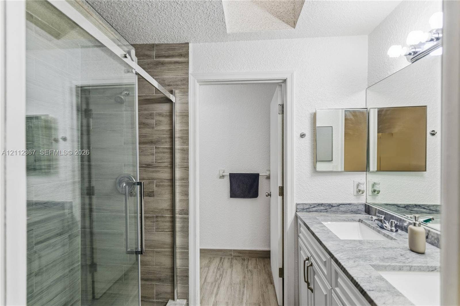 10803 Cypress Glen Drive, #10803, Coral Springs, FL 33071 Bathroom featuring a dual-sink vanity with stone-finish countertop, walk-in shower with glass enclosure, and wood-finish tile surround